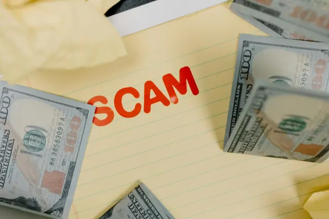 A shot of the word Scam on lined yellow paper surrounded by US dollar banknotes