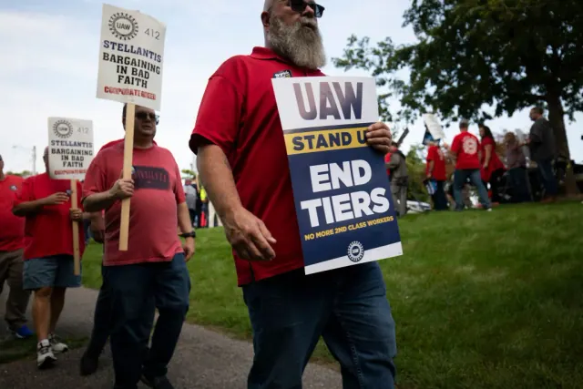 UAW picketers in red shirts carrying End Tiers signs