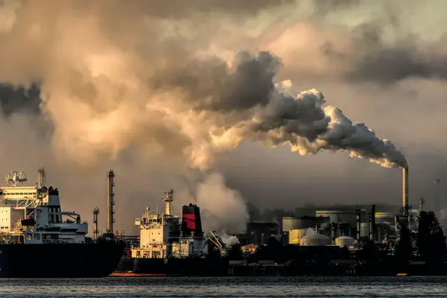 Industrial stacks releasing plumes beside a waterfront
