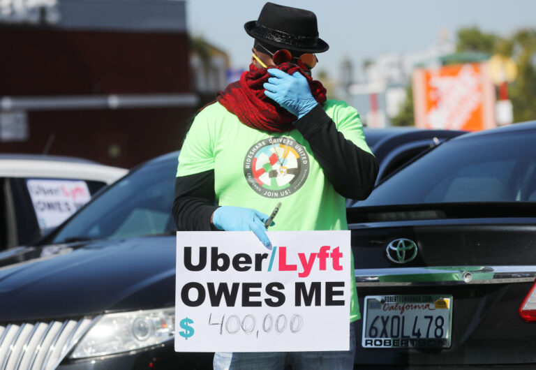 An Uber Driver Protesting for Employee rights holding a sight that says Uber and Lyft owe me.