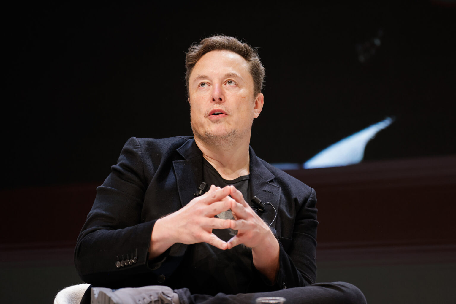 Elon Musk pitches hands together and looks up.