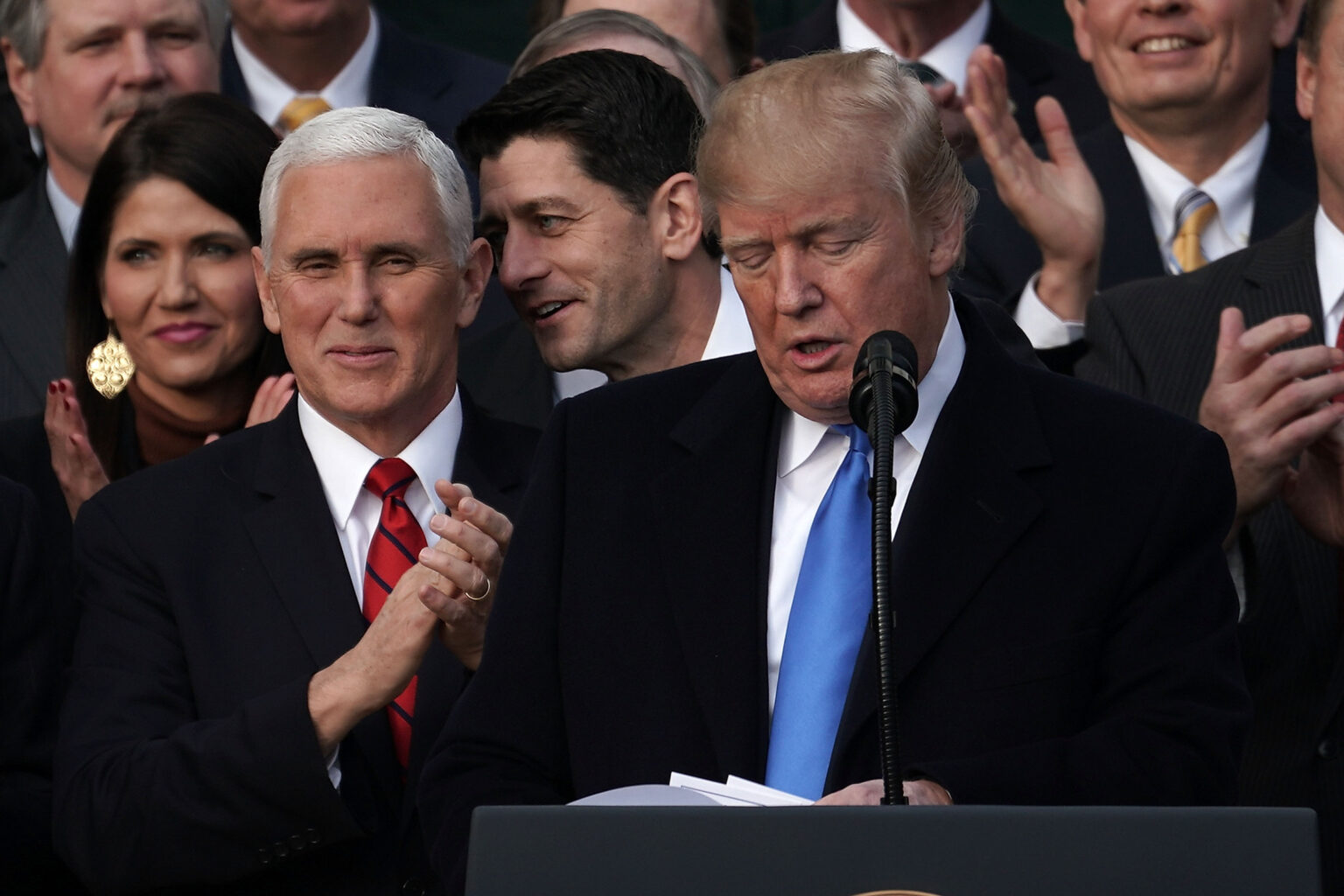 WASHINGTON, DC - DECEMBER 20: U.S. Speaker of the House Rep. Paul Ryan (R-WI) (3rd L) whispers to Vice President Mike Pence (2nd L) as President Donald Trump (R) speaks during an event to celebrate Congress passing the Tax Cuts and Jobs Act with Republican members of the House and Senate on the South Lawn of the White House December 20, 2017 in Washington, DC. The tax bill is the first major legislative victory for the GOP-controlled Congress and Trump since he took office almost one year ago.