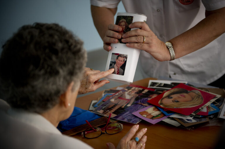 BARCELONA, SPAIN - AUGUST 02: Social worker Nuria Casulleres shows a portrait of Prince Charles, Prince of Wales to an elderly woman during a memory activity at the Cuidem La Memoria elderly home, which specializes in Alzheimer patients on August 2, 2012 in Barcelona, Spain. Nuria Casulleres, whose only daughter lives at home while attending University, is accustomed to 900 euros monthly for income. With The Catalan Government government cutbacks she is now only receiving 800 euro with rent taking 650 of that income. The Government currently cannot pay the July allocations to old age homes and others social services as a result of liquidity issues. According to reports, Spain's most indebted region, Catalonia, is not be able to pay 400 millions euros in grants. Approximately one hundred thousand social workers will see their salary cut by 40% to 50% while relatives of elderly home residents have had to help pay the salaries and expenses. (