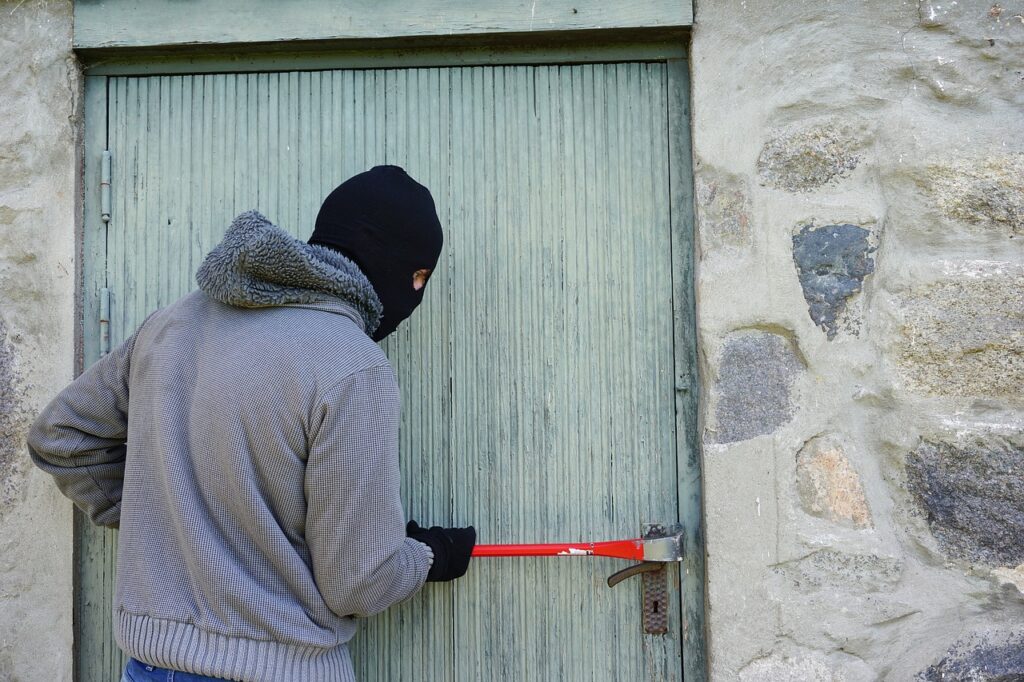 man with a ski mask and crowbar prying at a door