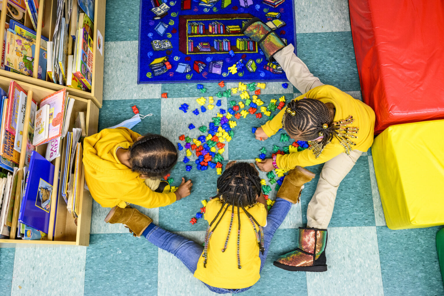 areil shot of three kids dressed in yellow playing with colorful blocks in a childcare facility