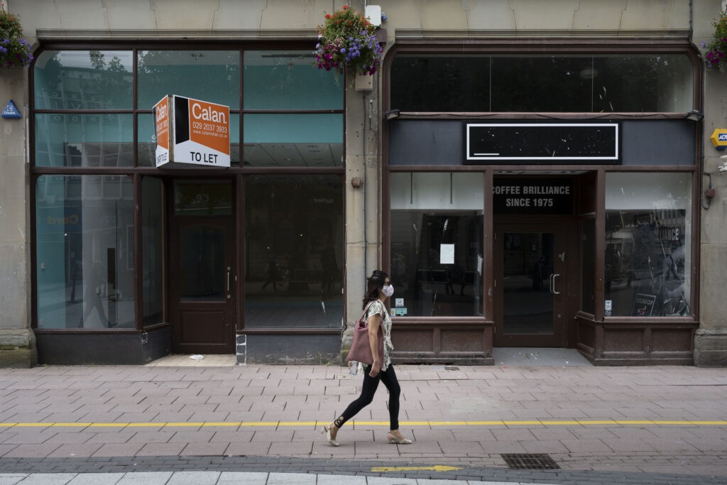 CARDIFF, UNITED KINGDOM - AUGUST 04: A woman wearing a surgical face mask walks passed closed shops on Queen Street on August 4, 2020 in Cardiff, United Kingdom. Coronavirus lockdown measures continue to be eased as the number of excess deaths in Wales falls below the five-year average. From this week up to 30 people can meet outdoors and pubs, restaurants and cafes can open to customers indoors.