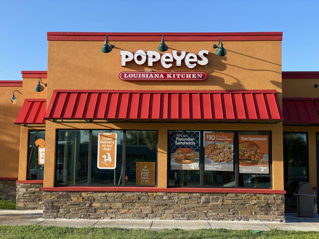 A store front of a Popeye's Louisianan kitchen against a blue sky. 